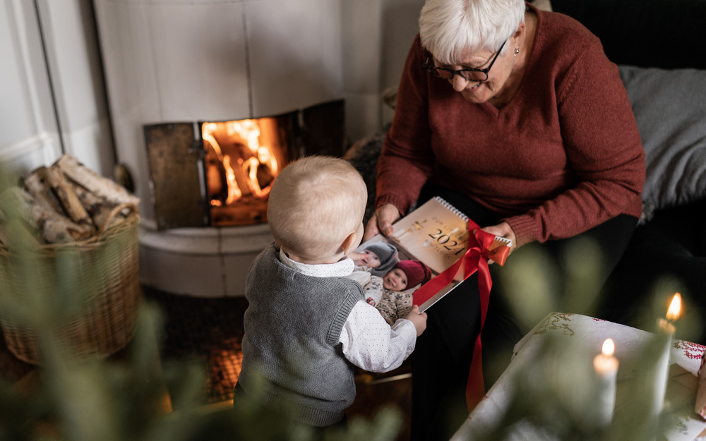 A small child giving a photo calendar as a Christmas present to his grandmother