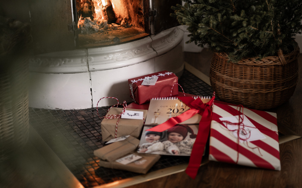 Ein Fotokalender und fünf eingepackte Geschenke vor einem Kachelofen, in dem ein Feuer brennt